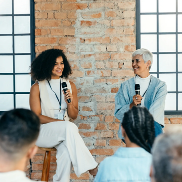 Two women speaking on microphones in front of an audience during a discussion.