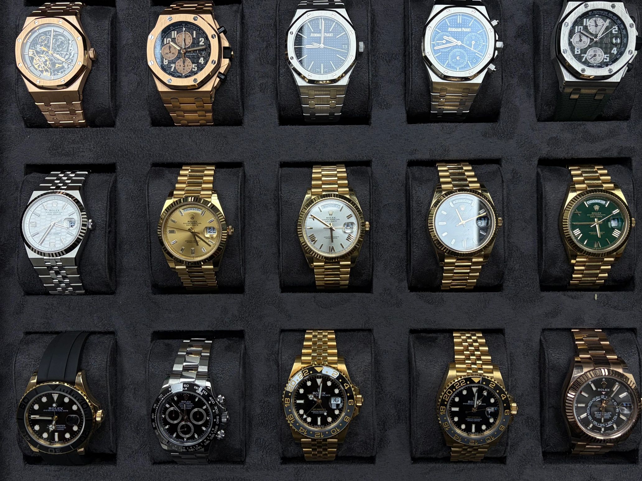 Luxury watches collection featuring Audemars Piguet and Rolex in a black display case.