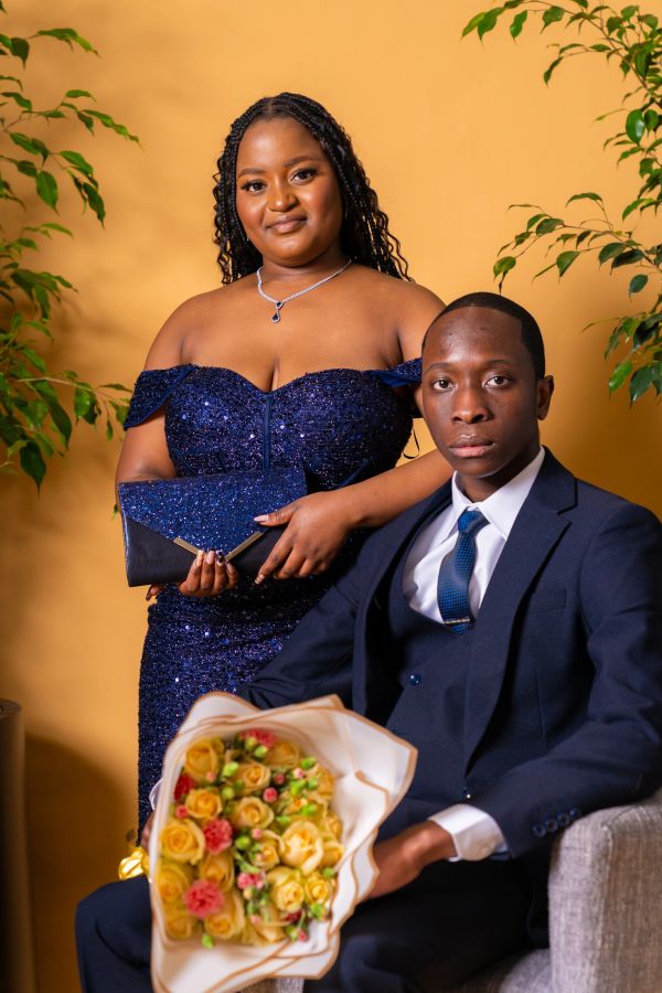 A young couple dressed formally, the woman holding a clutch and the man holding a bouquet.