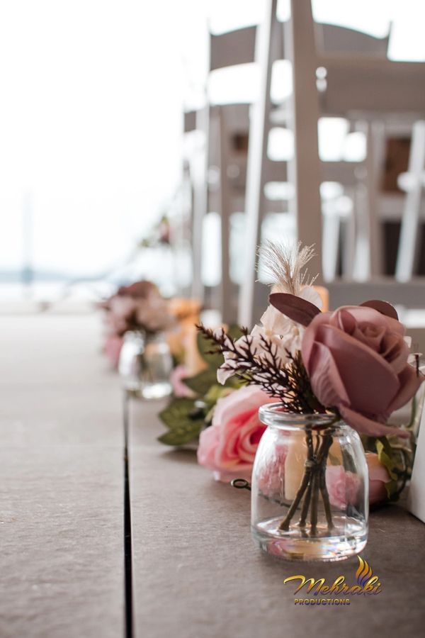 Delicate pink roses in small glass vases line an aisle with white chairs.