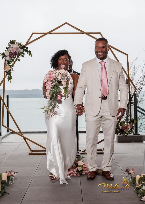 Joyful couple holding hands after wedding ceremony by lakeside.