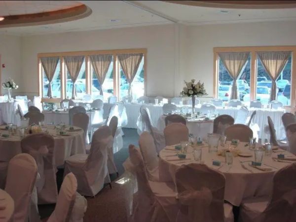 Elegant banquet hall set up with white covered chairs and floral centerpieces.
