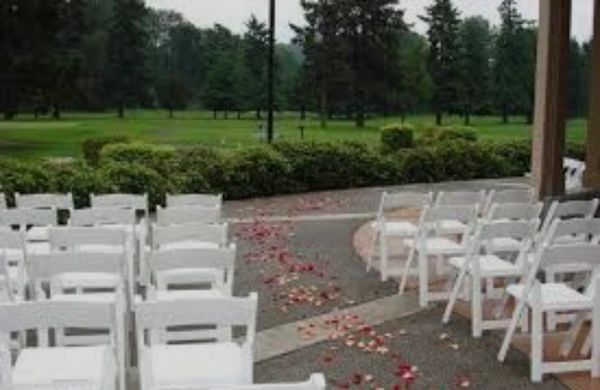 Outdoor wedding setup with white chairs and rose petals on the ground.