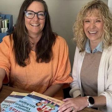Two women smiling together at a table with books.