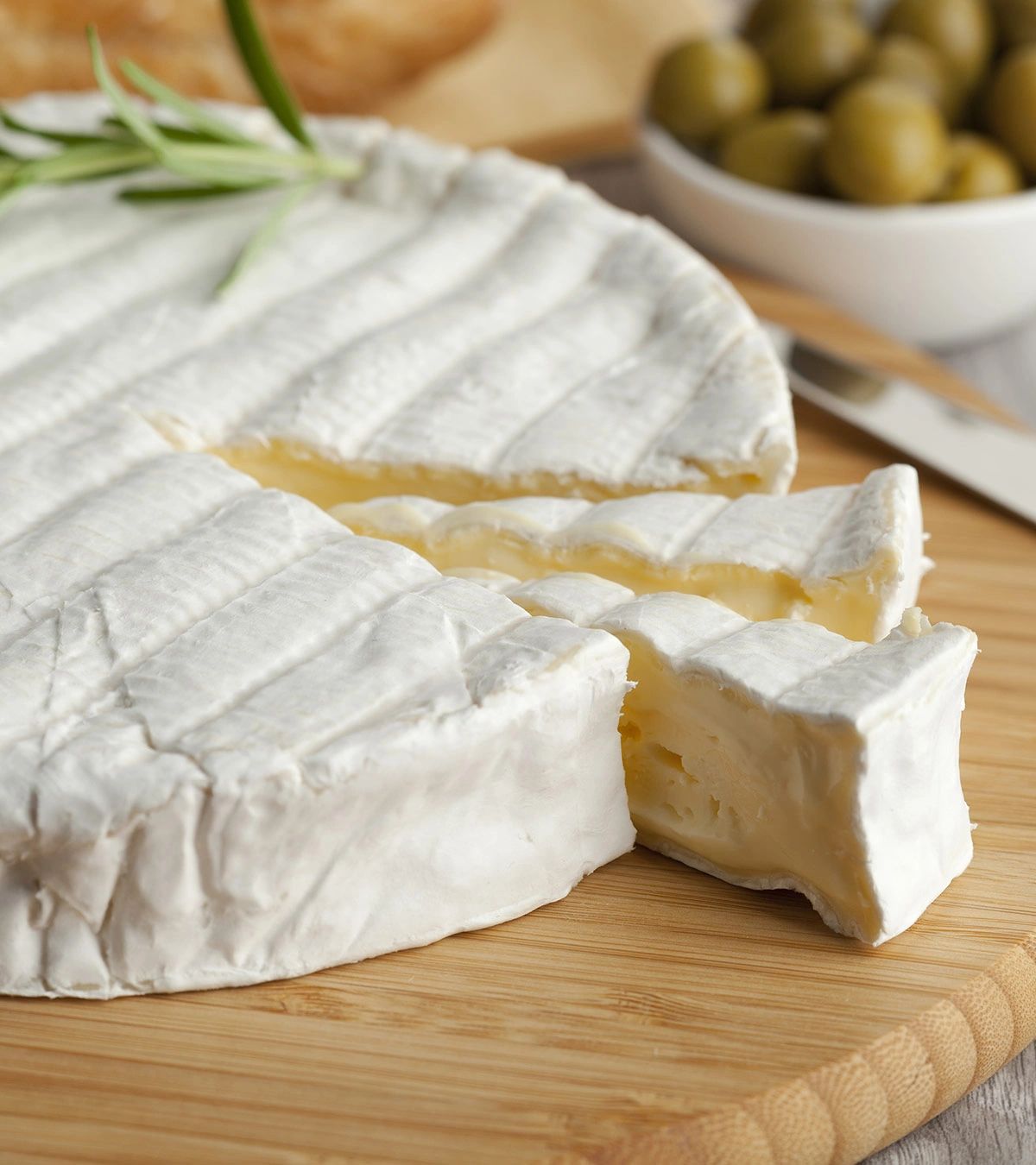 A creamy wheel of brie cheese with a slice cut out on a wooden board.