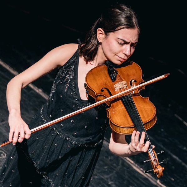 Woman deeply focused playing violin on stage in a black dress.