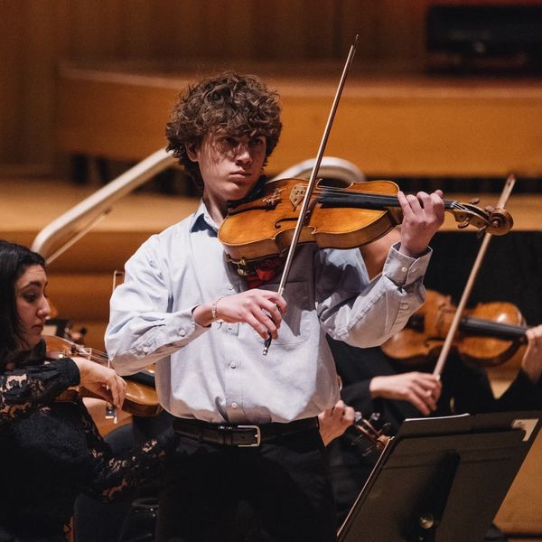 Young man passionately playing violin in an orchestra.