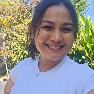 A smiling woman outdoors with greenery in the background.