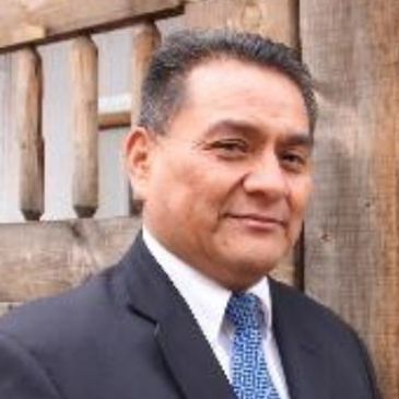Man in a suit and tie standing outdoors near wooden structures.