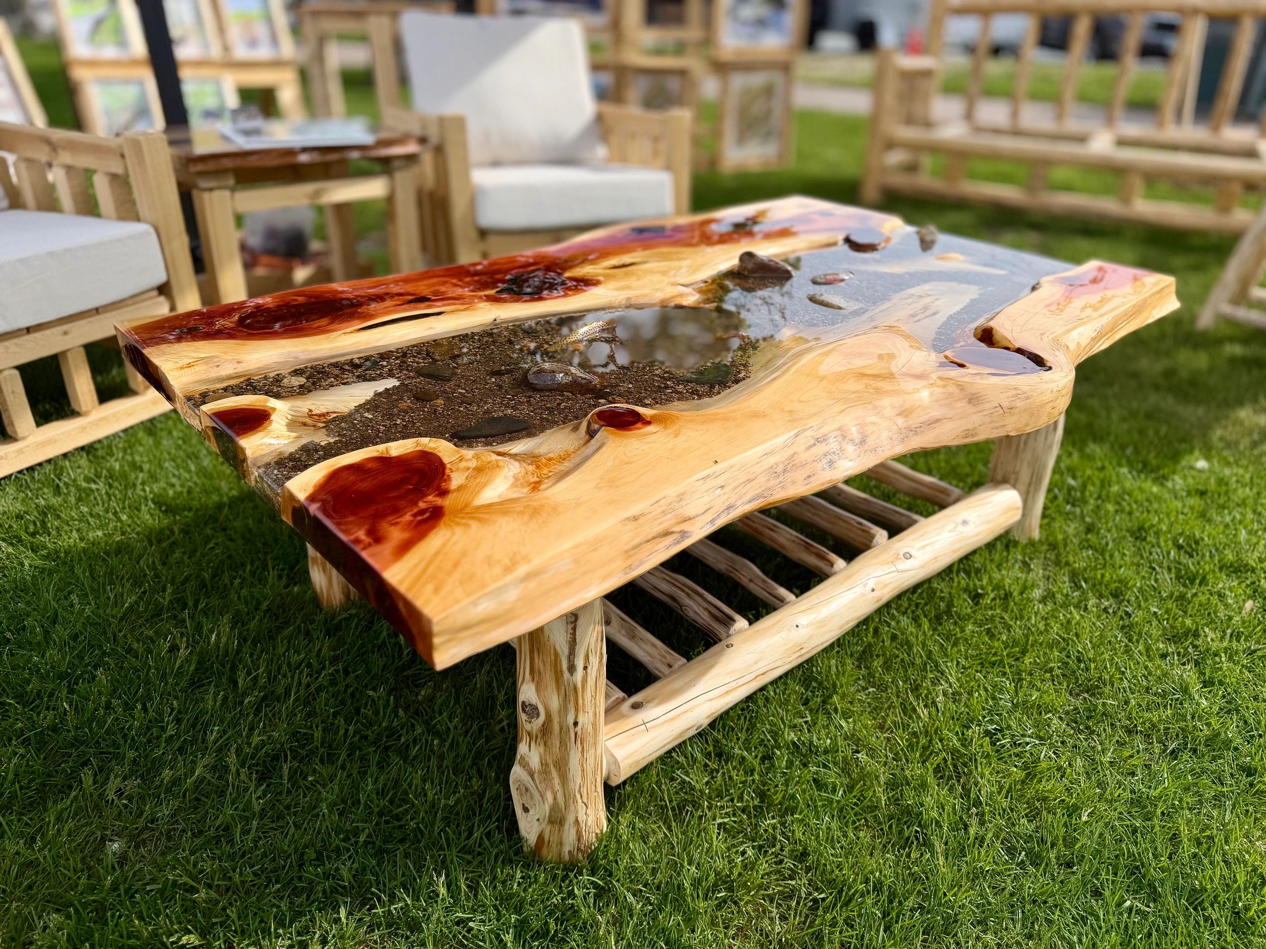 Handcrafted wooden table with a resin river and embedded stones on a grassy lawn.