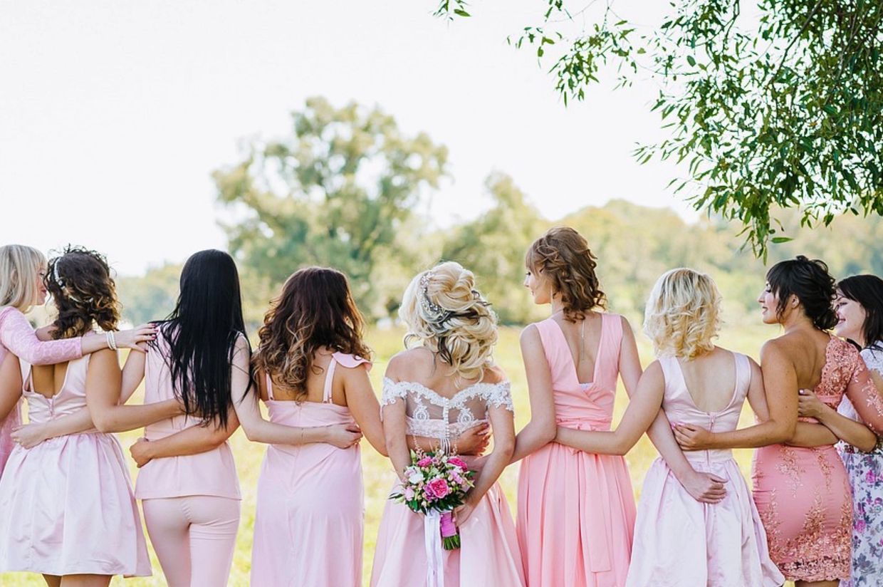 Bridesmaids in pink dresses embrace the bride outdoors.