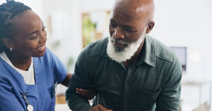 A nurse warmly assisting an elderly man with a smile.
