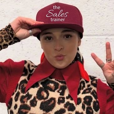 Person wearing a red cap with 'the Sales trainer' text and making a peace sign.