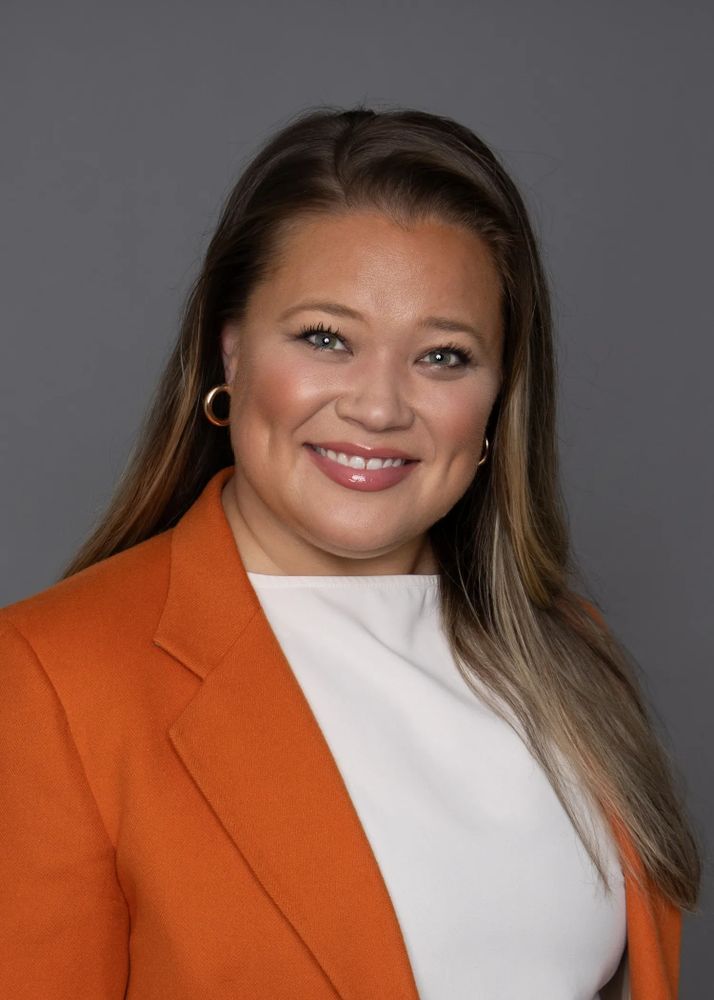 Smiling woman in an orange blazer and white top against a gray background.