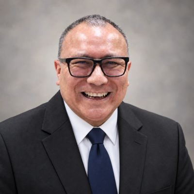Hombre sonriente con traje negro y corbata azul.