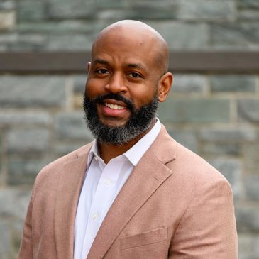 Confident man smiling in a beige blazer outdoors.