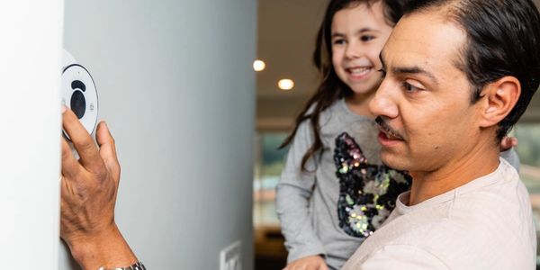 Father holding daughter adjusting a wall thermostat