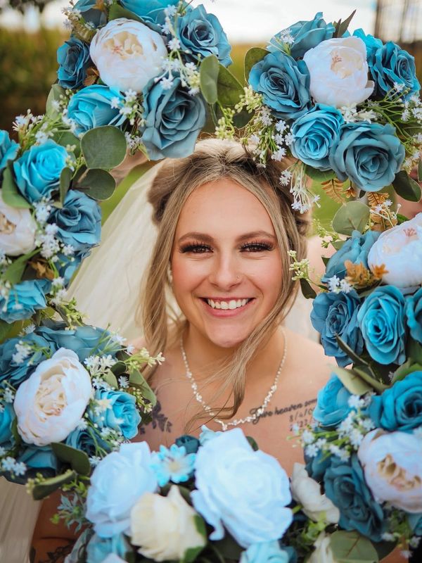 Smiling bride framed by heart-shaped blue and white flower arrangement.