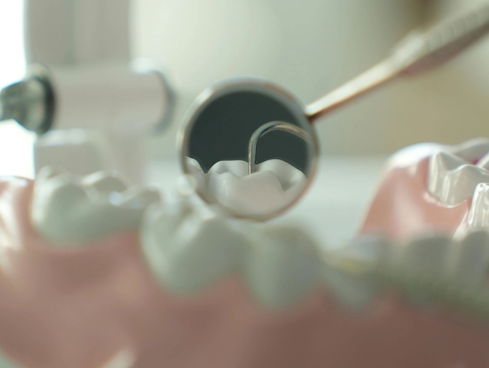 Close-up of dental mirror reflecting teeth and dental probe on a dental model.