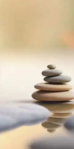 Stacked smooth stones balanced on a reflective surface with a soft background.