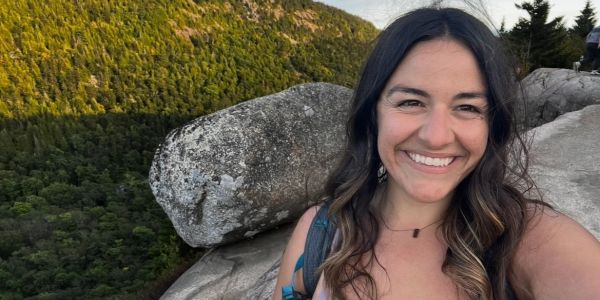 Smiling woman hiking in a mountainous area during sunset.