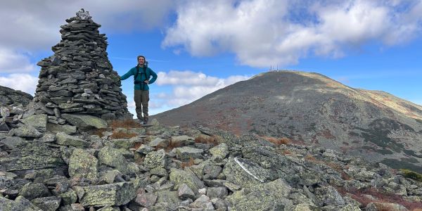 Hiker standing by a stone cairn on a rocky mountain peak.