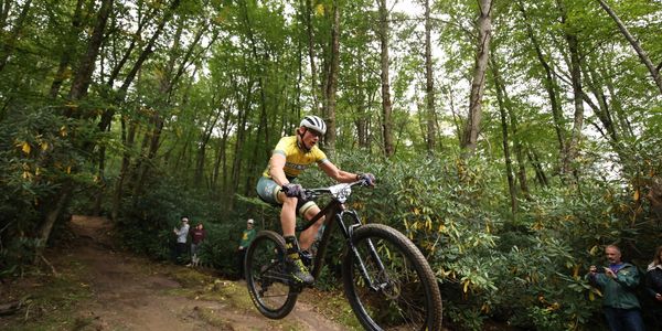 Mountain biker in yellow jersey jumps on forest trail.