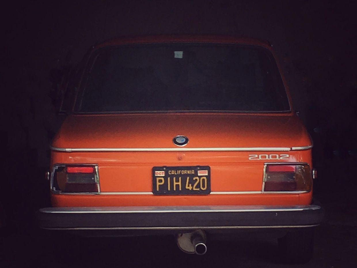 Rear view of an orange BMW 2002 with a California license plate in a dark garage.