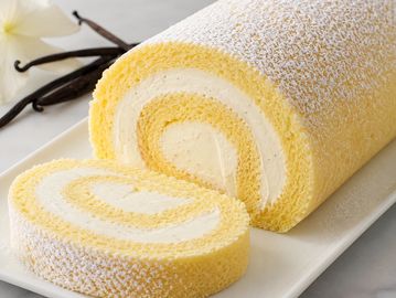 A vanilla Swiss roll cake dusted with powdered sugar on a white plate.