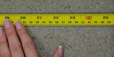 Hand with manicured nails holding a yellow measuring tape on concrete.