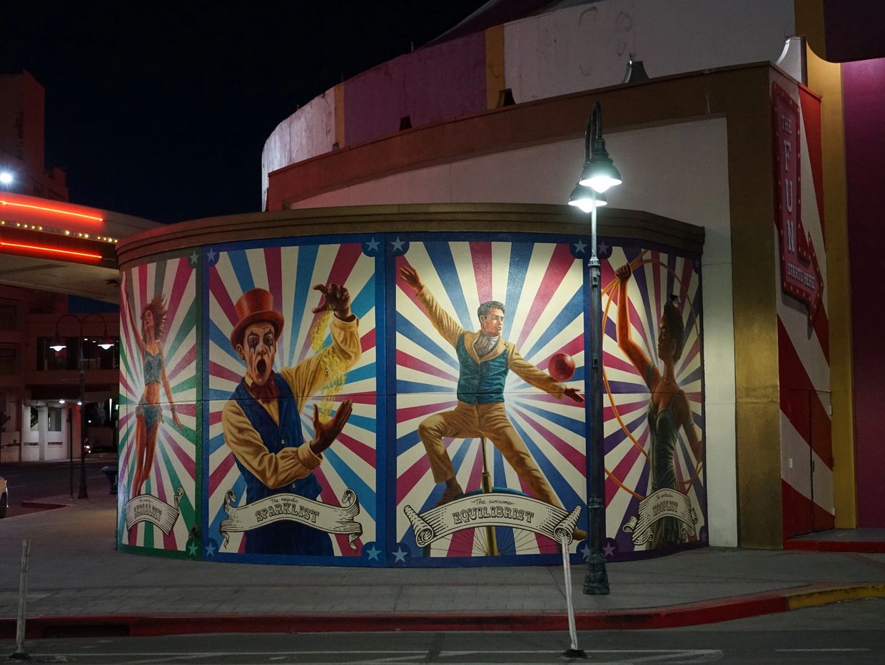 Nighttime mural of circus performers on a building corner.