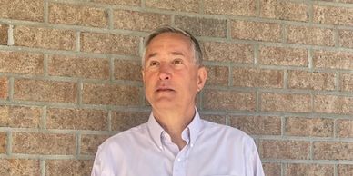 Man in white shirt standing against a brick wall, looking upward.