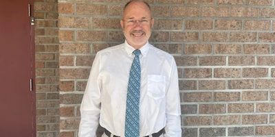 Smiling man in white shirt and blue tie standing by brick wall.