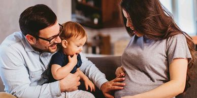 Young toddler with his mother and father touching pregnant mother's stomach