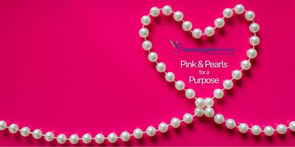 Pearl necklace shaped into a heart on a vibrant pink background for a charitable cause.