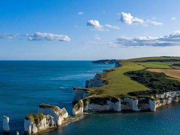 Cliffs overlooking a calm blue sea under a partly cloudy sky.