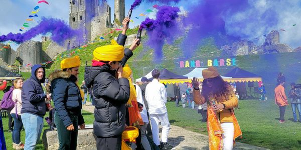 People celebrating with purple smoke flares at a colorful outdoor festival.