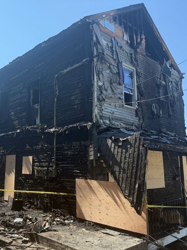 Fire-damaged two-story house with boarded windows and charred walls.