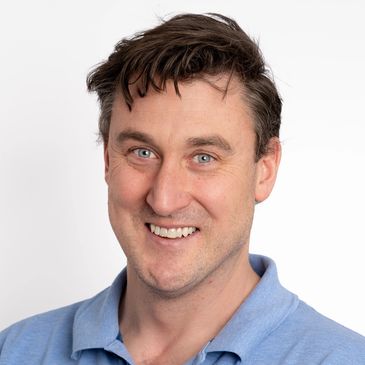 Smiling man with blue eyes and brown hair in a blue shirt.