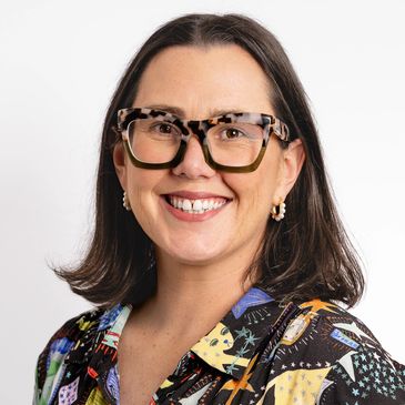 Smiling woman with dark hair and large tortoiseshell glasses.