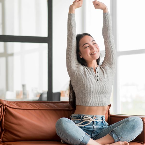 Young woman stretching happily on a couch in a bright room.