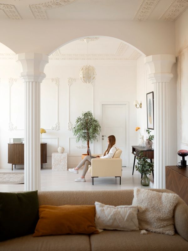 A woman sits in a bright, elegant living room with classical columns and modern decor.