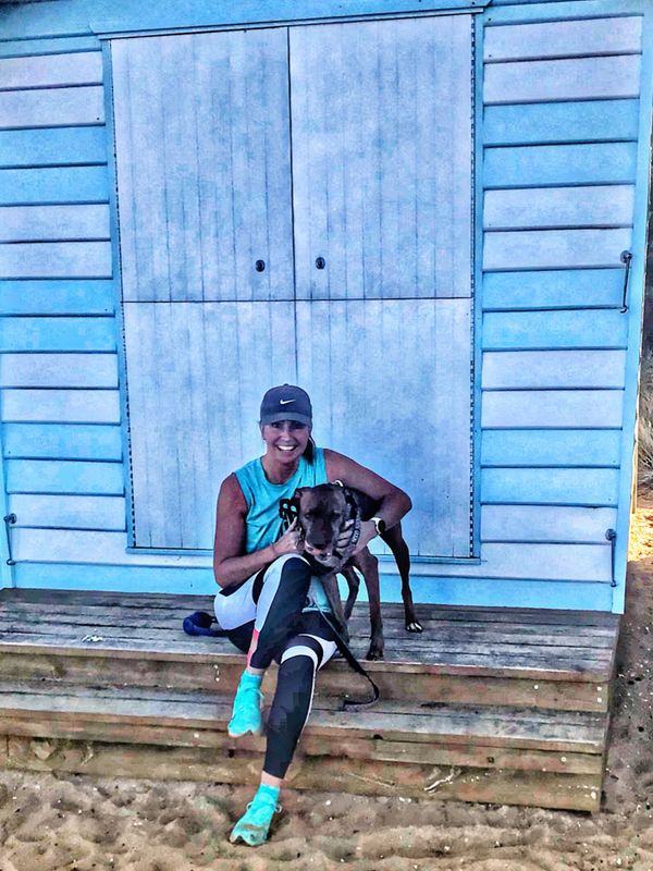 A woman in athletic wear sits on wooden steps with her dog in front of a blue building.