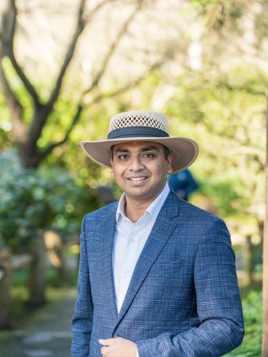 A man in a blue suit and straw hat smiling outdoors.