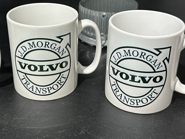 Two white mugs with J.D. Morgan Volvo Transport logo on a black surface.