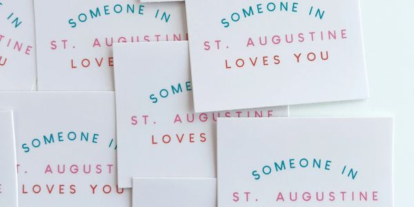 Cards with the phrase 'Someone in St. Augustine Loves You' scattered on a white surface.