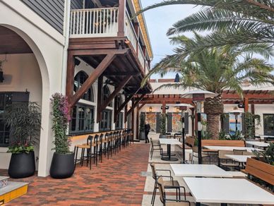 Outdoor seating area with tables, chairs, and palm trees in a restaurant courtyard.