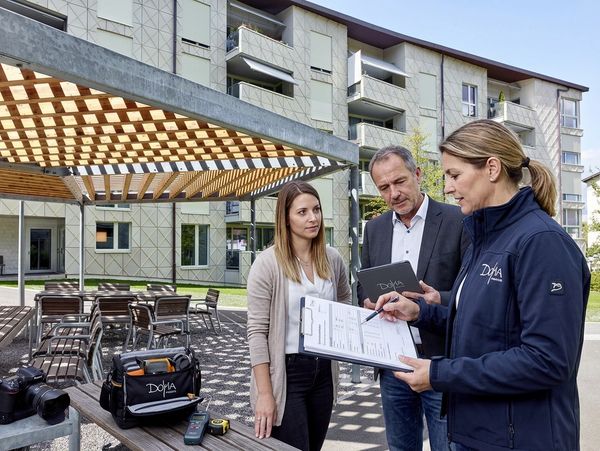 Three professionals discussing documents outdoors near a modern building.