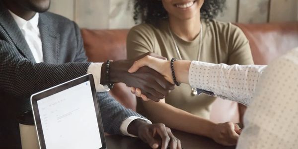 Two people shaking hands during a business meeting with a third person smiling.