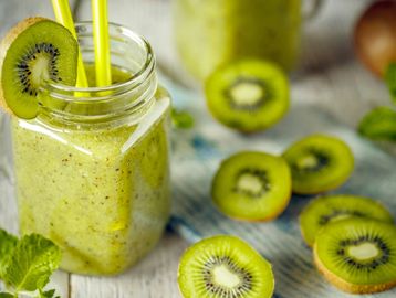 Fresh kiwi smoothie in a mason jar with kiwi slices and yellow straws.